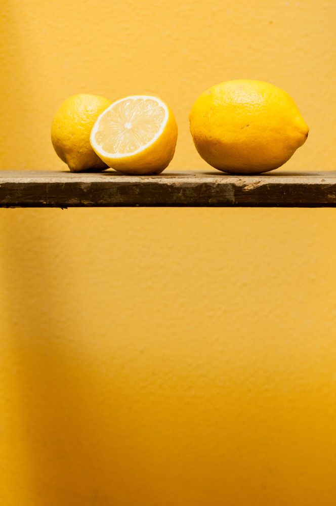 Dos frutas amarillas apoyadas sobre una barra metálica frente a fondo amarillo.
